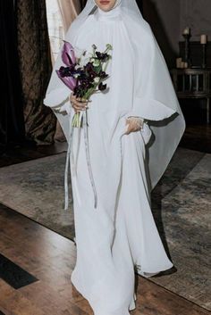 a woman in a white dress and veil holding flowers