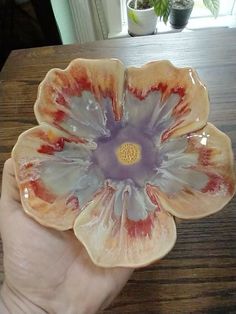 a hand holding a flower shaped dish on top of a wooden table