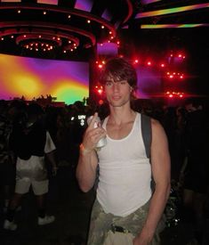 a young man standing in front of a large screen at a concert holding a drink