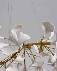 a chandelier with white flowers hanging from it's sides and gold accents