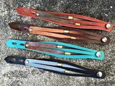 four different colored leather hair clips sitting on top of a stone floor next to each other