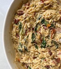 a bowl filled with pasta and spinach on top of a white tablecloth next to a wooden spoon