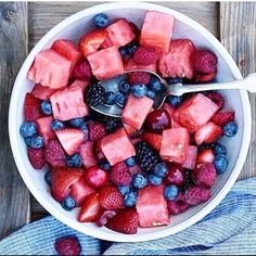 a bowl filled with watermelon, blueberries and raspberries on top of a wooden table