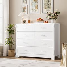 a white dresser with pictures on the wall above it and a potted plant next to it