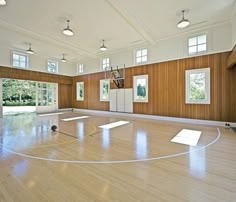 an indoor basketball court with hard wood flooring and white painted walls, surrounded by windows