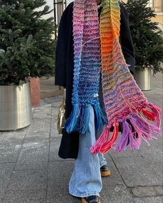 a woman is walking down the street wearing a multicolored knitted scarf with fringes