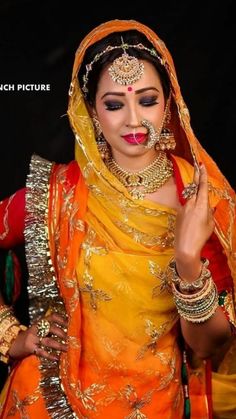 a woman in an orange and yellow outfit with jewelry on her head, wearing a red nose ring