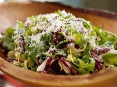 a wooden bowl filled with lots of green and red salad