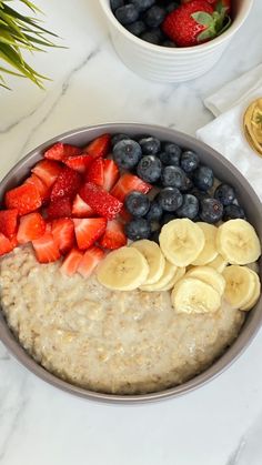 a bowl of oatmeal with sliced bananas, strawberries and blueberries