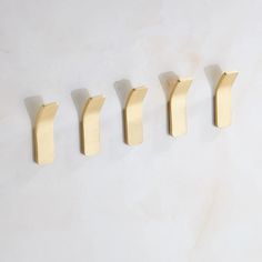 five brass hooks hang on a white marble wall, each with one hook in the shape of an arrow