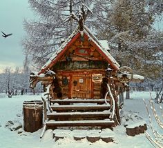 a log cabin in the middle of winter with snow on the ground and birds flying around