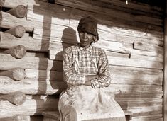 an old photo of a woman sitting on a log cabin bench with her arms crossed