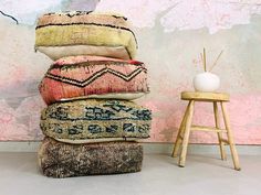 a stack of pillows sitting on top of a wooden stool in front of a wall