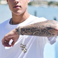 a man with a tattoo on his arm pointing to the side while wearing a white t - shirt