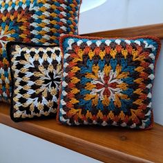 three crocheted square pillows sitting on top of a wooden shelf next to each other