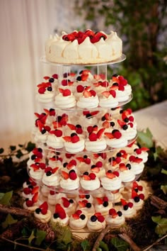 a three tiered cake with white frosting and red berries on the top is surrounded by greenery