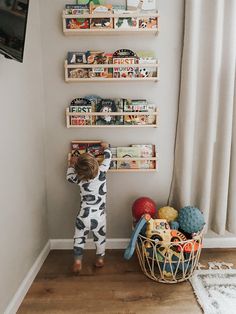 a little boy standing in front of a wall mounted book shelf