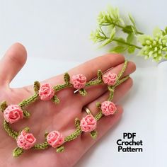 crocheted pink flowers are on the palm of a person's left hand