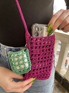 a person holding a cell phone in a crocheted case with two handles and straps