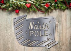 a metal sign with the words north pole on it next to christmas wreaths and garland