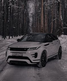 a white range rover driving down a snowy road in front of trees and snow covered ground