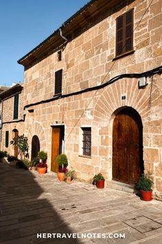 an old stone building with potted plants on the outside and wooden doors in front