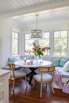 a dining room table with chairs and a bench in front of two windows that have flowers on them