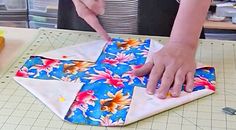 a woman is making a cross out of fabric on a cutting board with a knife