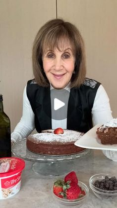 a woman sitting at a table with two cakes on it