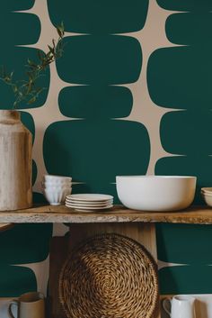 bowls, plates and vases are sitting on a shelf in front of a green wall