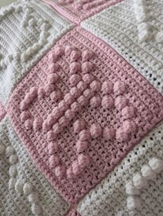 a pink and white crocheted blanket sitting on top of a bed next to a pillow