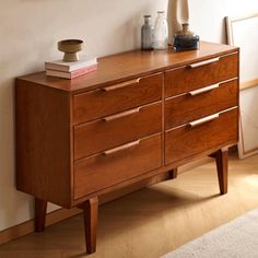 a wooden dresser with two vases on top of it next to a white wall