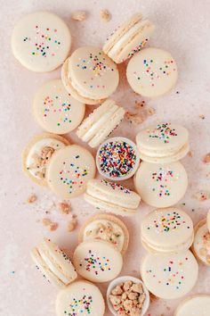 white frosted macaroons with sprinkles and nuts on a pink background