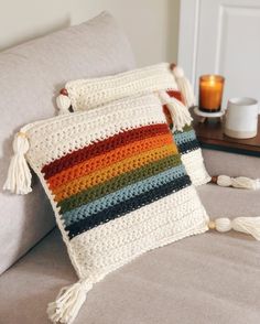 two crocheted pillows sitting on top of a couch next to a cup and candle