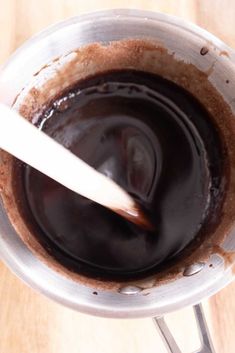 a wooden table topped with a metal bowl filled with liquid and a spoon in it