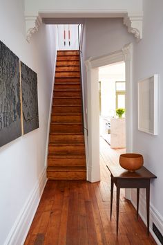 a wooden staircase leading up to a living room with white walls and wood flooring