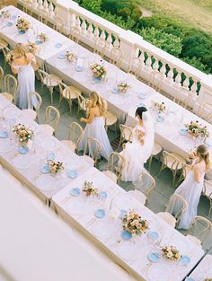 several women in white dresses sitting at long tables with blue and white plates on them