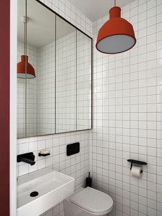 a white toilet sitting next to a bathroom sink under a red hanging light above it