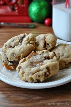 chocolate chip cookies on a white plate next to a glass of milk and christmas decorations