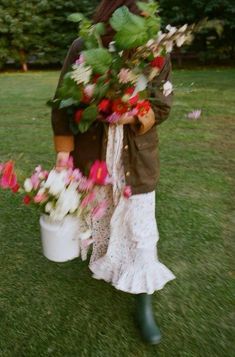 a woman holding flowers in her hands and walking through the grass with two buckets full of flowers