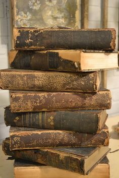 a stack of old books sitting on top of each other in front of a painting