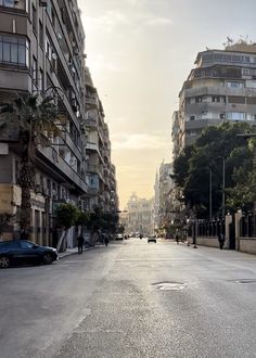 an empty city street with cars parked on both sides and tall buildings in the background