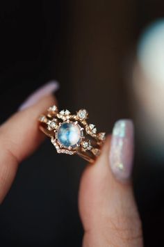 a woman's hand holding a gold ring with an oval blue stone in it