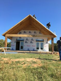 two men are working on the roof of a house under construction, while another man stands nearby