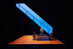 three people sitting on a bench in front of a stair case with blue light coming from the top