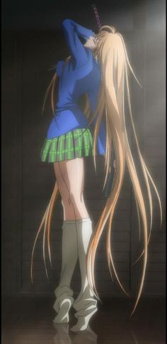 a woman with long blonde hair standing in front of a brick wall wearing a blue shirt and green skirt