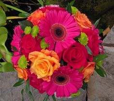 a bouquet of colorful flowers sitting on top of a stone wall next to some plants