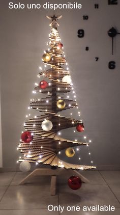 a christmas tree made out of books with lights and ornaments on the top is displayed in front of a wall clock