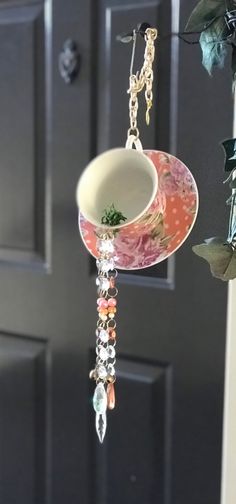 a teacup hanging from a hook on a door handle with flowers in the background