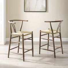 two wooden chairs sitting next to each other in front of a painting on the wall